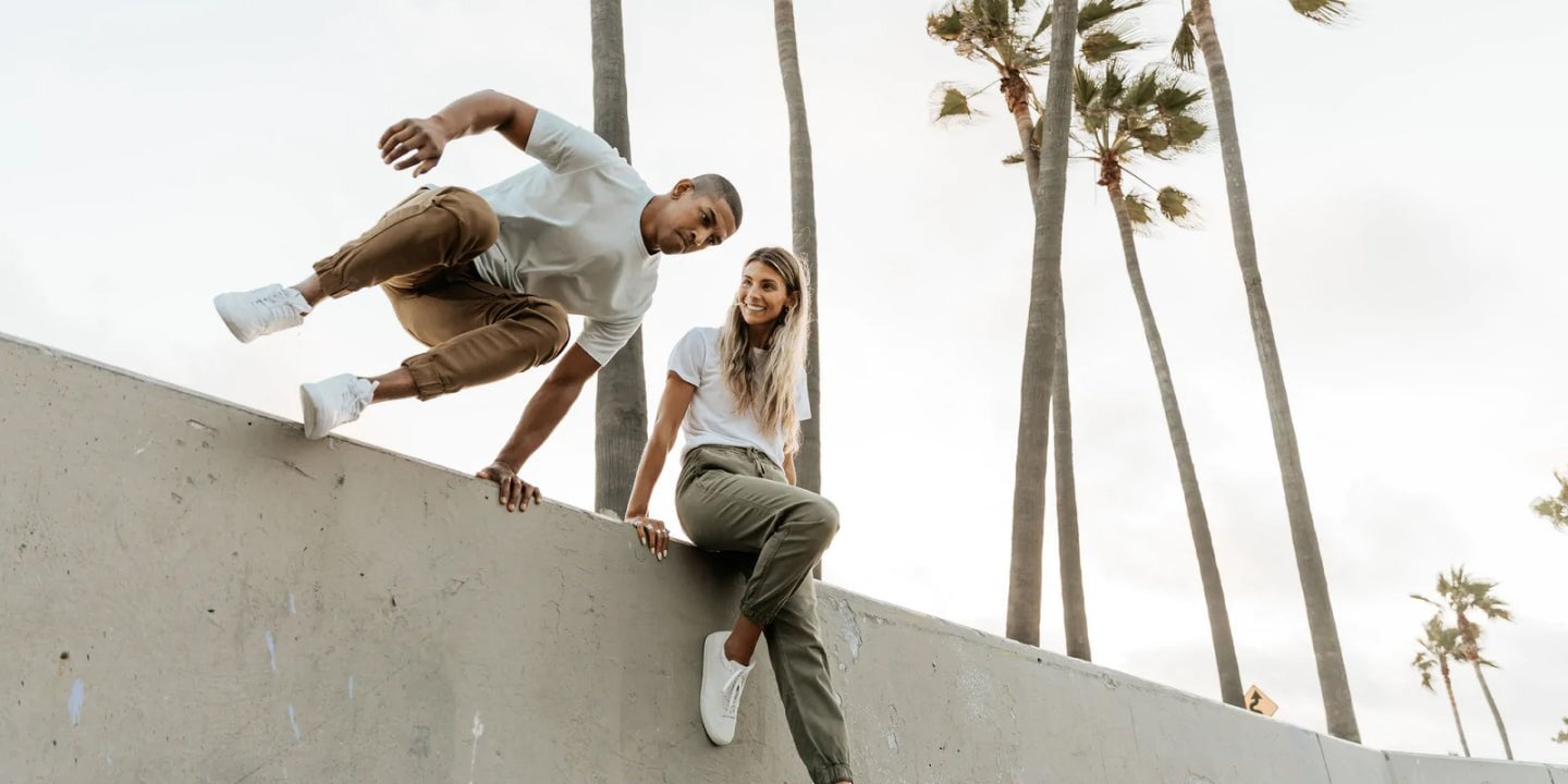 A man and woman wearing DUER joggers jumping over a concrete wall