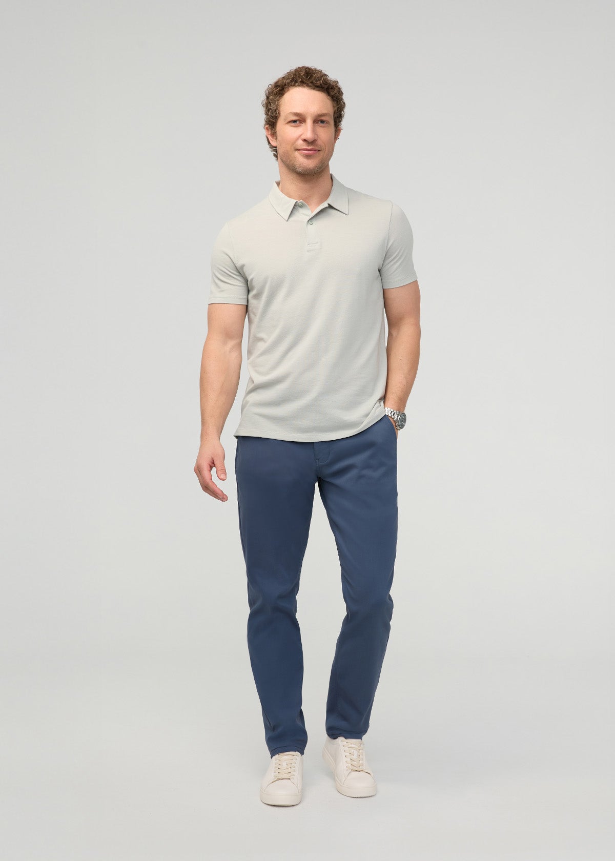 Man wearing light gray polo shirt and navy blue tapered trousers with cream sneakers.