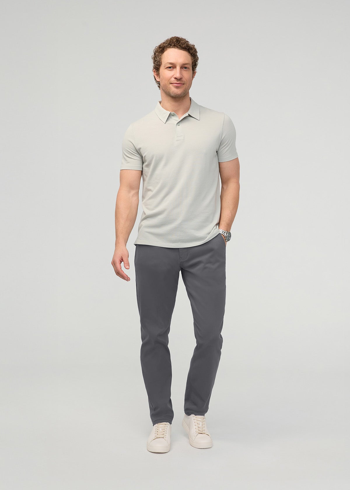 Man wearing gray relaxed taper trousers with a light gray polo shirt and cream sneakers.