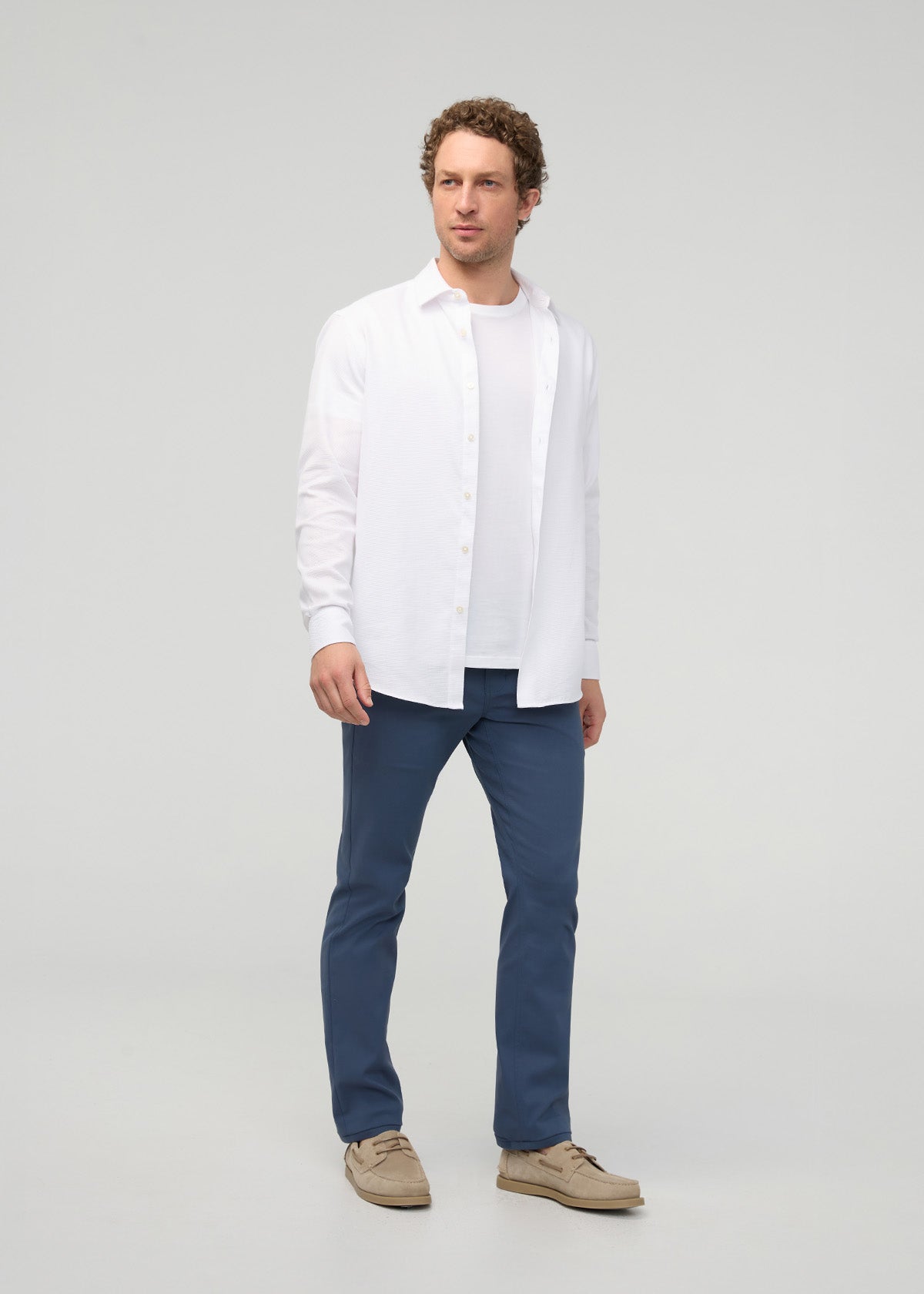 Man wearing heritage blue slim straight trousers with white button-up shirt and tan shoes.