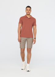 Man wearing a terracotta polo shirt and sandstone shorts with white sneakers.
