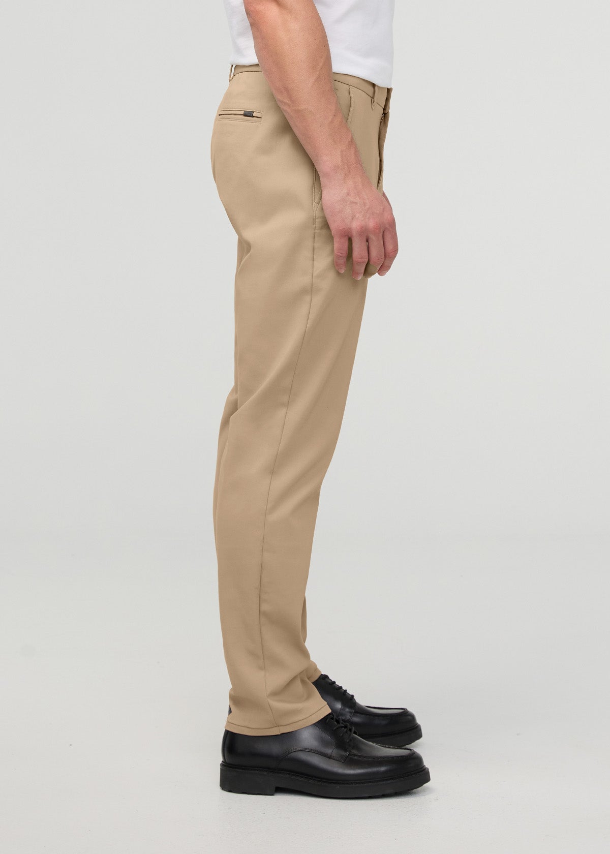 Beige tapered trousers with relaxed fit worn with white shirt and black platform shoes, shown from the side.
