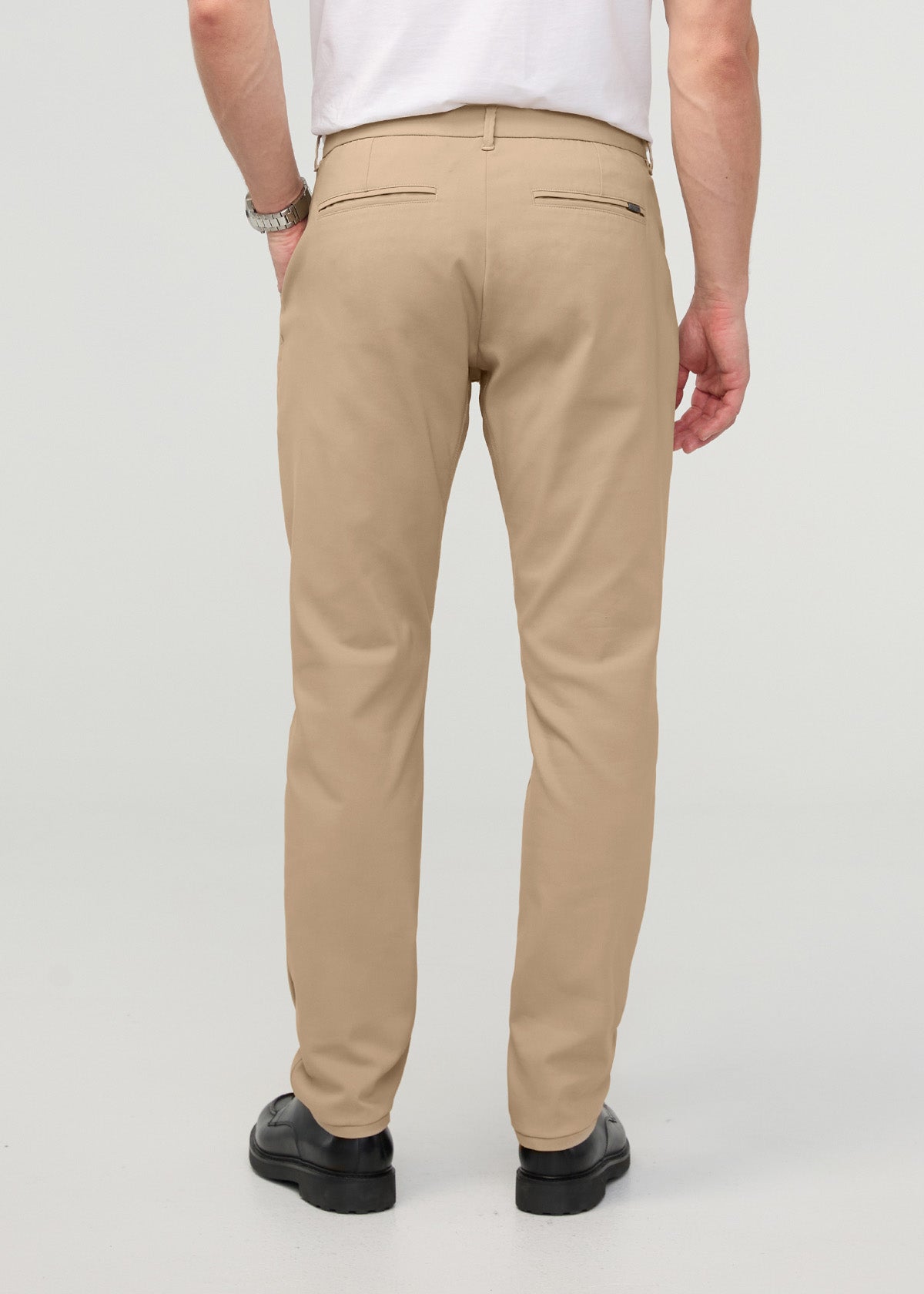 Beige relaxed taper trouser with back zip pockets, shown from behind on a model wearing a white shirt.