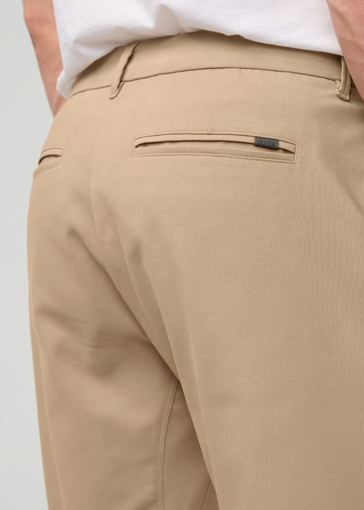 Desert khaki relaxed taper trouser with flat front waistband and back welt pocket, worn with white shirt.