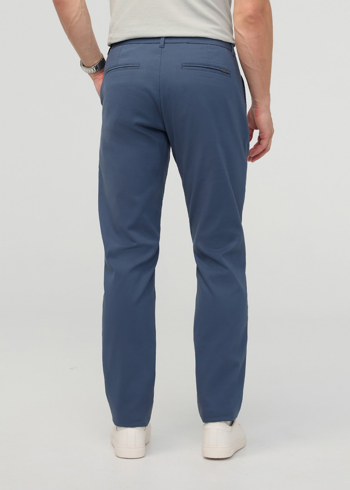 Man wearing blue heritage taper trousers with cream shirt, shown from behind with hands in pockets.