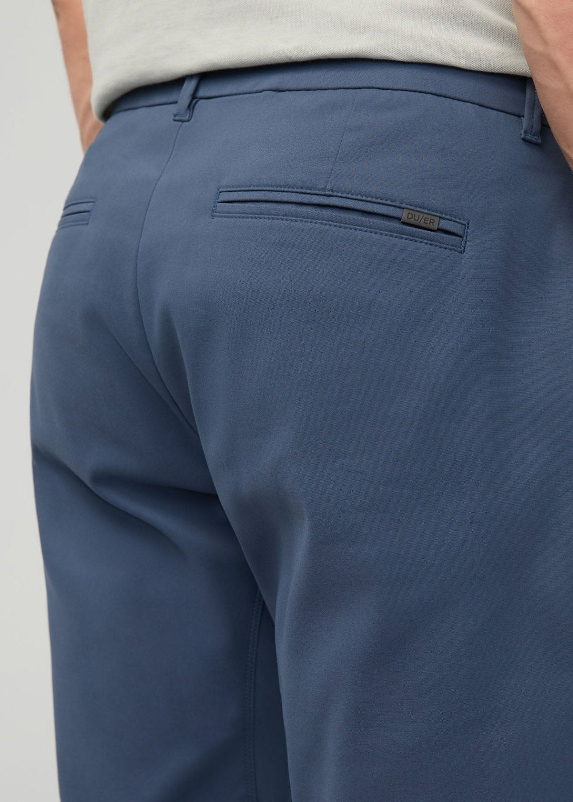 Blue relaxed taper trousers with back welt pocket and brand label, shown from rear on model wearing cream top.