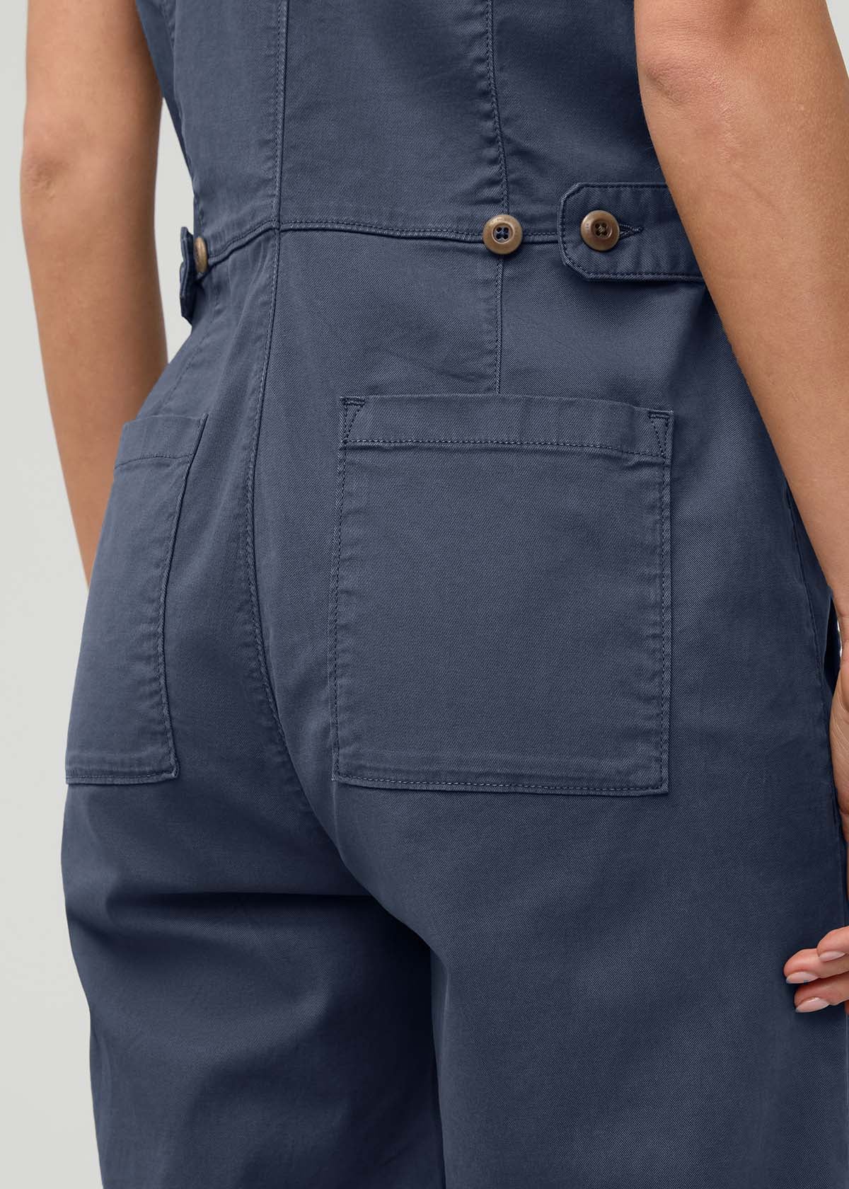 Heritage blue sleeveless boiler suit with cargo pockets, wooden buttons, and belt straps at waist.