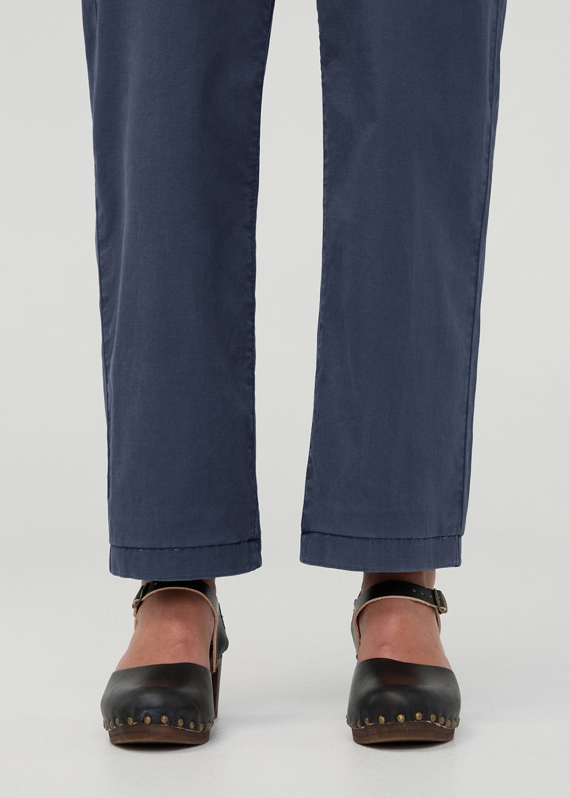 Navy blue boiler suit pants with cuffed hems, shown from waist down with black studded clogs.