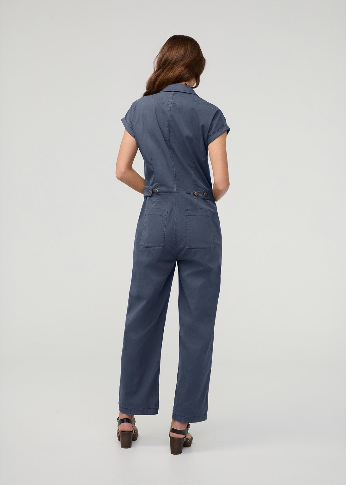 Woman wearing a blue boiler suit with short sleeves, collar, and utility pockets, shown from behind.