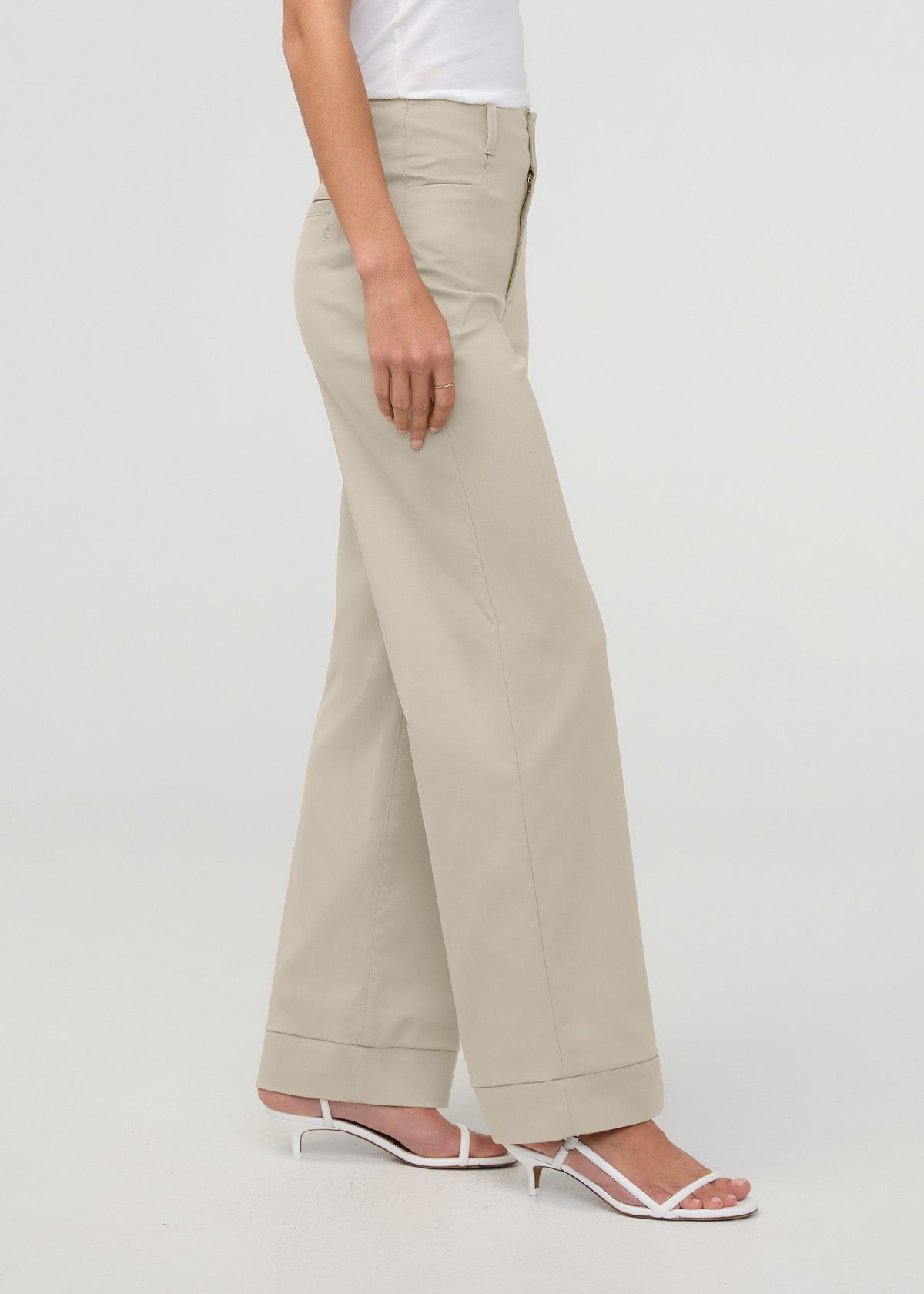 Beige high-rise trousers with cuffed hem worn with white sandals, shown from side view.