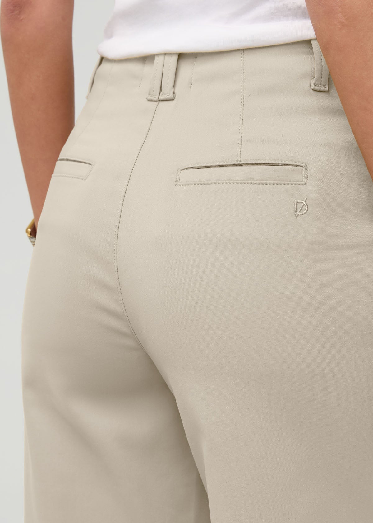 Sandstone high-rise trouser with belt loops, front pockets, and back welt pockets on model wearing white tank top.
