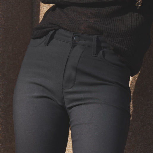 A person from the waist down, wearing high-waisted, fitted black pants and a dark knit top.