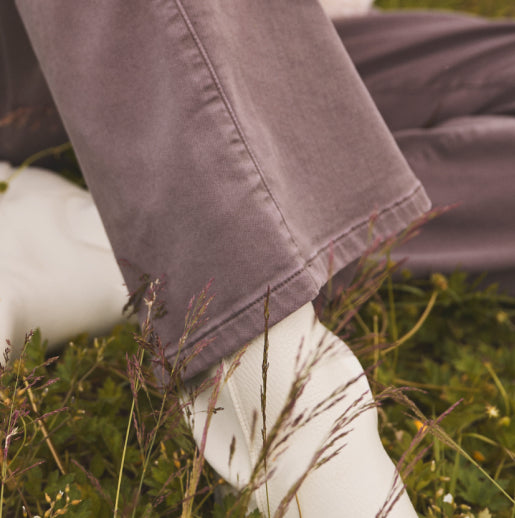 A person sitting in the grass, close-up of their brown wide leg pants from the shin down.