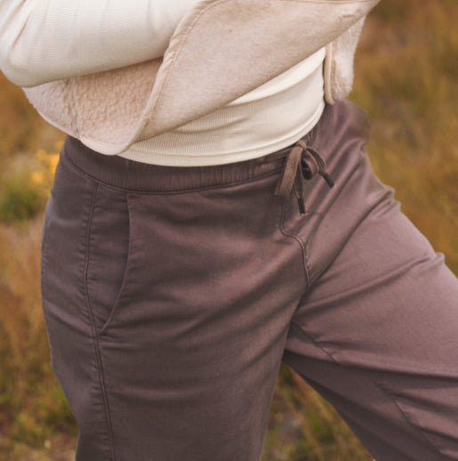 A person wearing brown drawstring pants, standing in field.