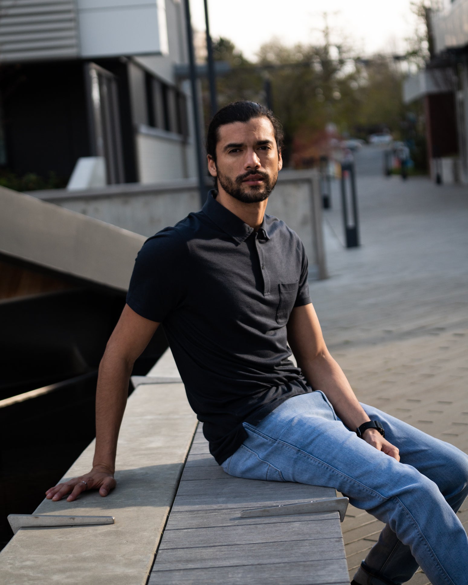 man wearing a black soft lightweight polo sitting outside in light wash jeans